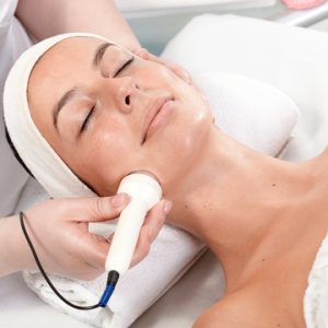 Young woman laying eyes closed, receiving facial beauty treatment in beauty salon.